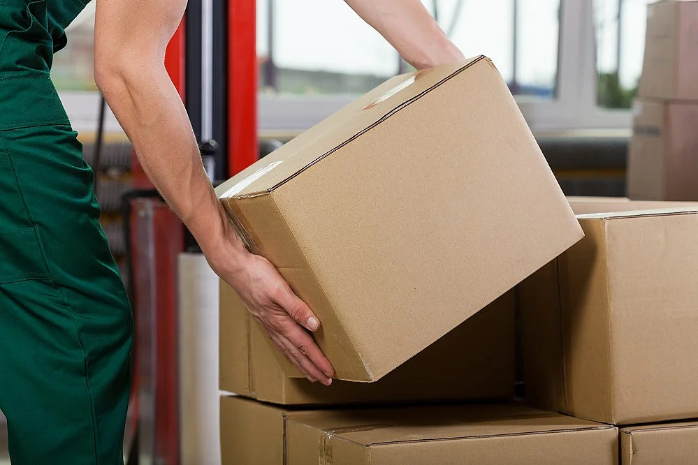 Eine Person hebt ein Paket von einem größeren Stapel Pakete herunter